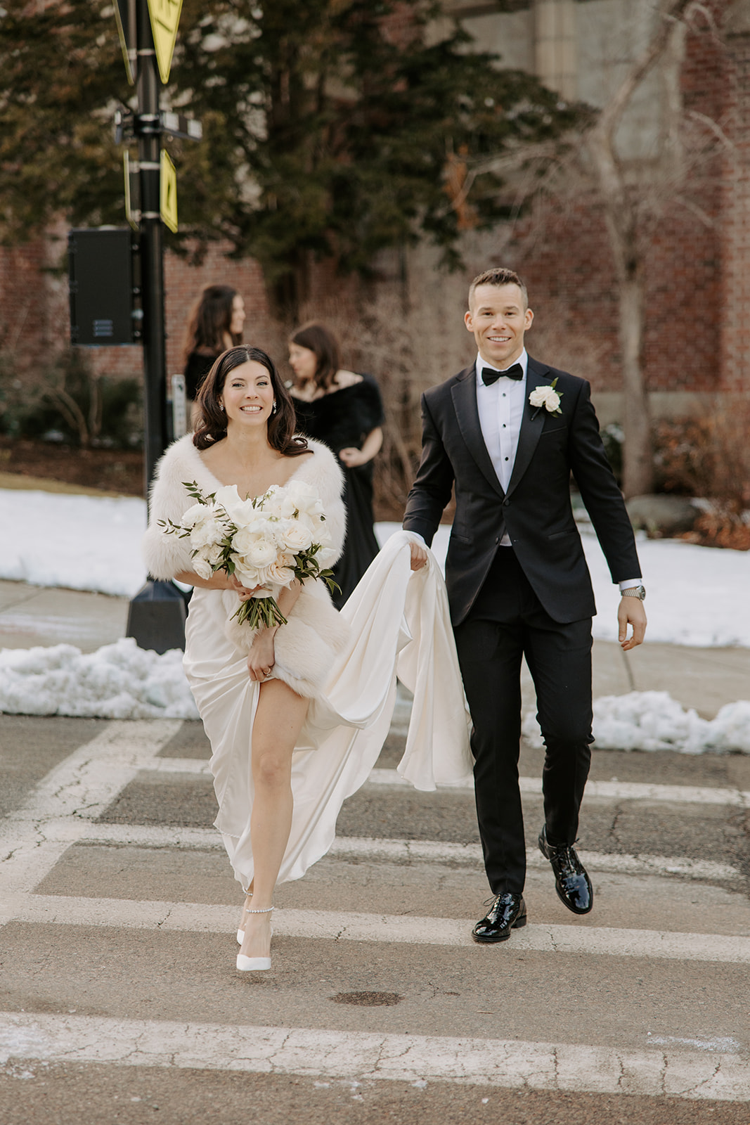 Groom holding bride's dress up while they walk across a crosswalk for their winter wedding.