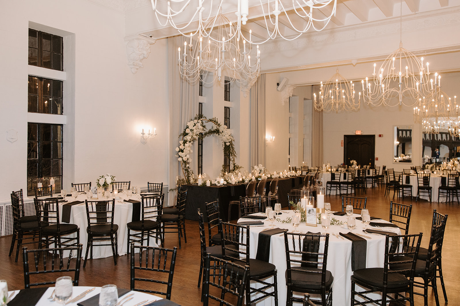Vintage ballroom set up with white table clothed tables, black wooden chairs with the head table and wedding arbor in the background at Alden Castle.